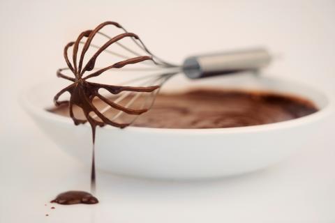 Image of a whisk propped on a bowl of chocolate, with chocolate dripping off of the whisk. 