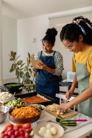 Image depicting an individual preparing sliced boiled eggs, and another looking at a clip board and holding a pen. 