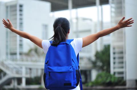Back-facing youth wearing a blue backpack with arms held out high. 
