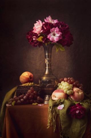 Still life photograph of flowers in a vase and fruit on a table.