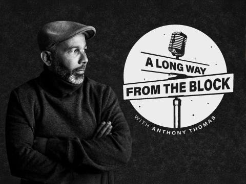 A black and white photograph of a black American man wearing a black long sleeve sweater and a hat is standing in front of a black backdrop. He looks to his left. To the left is his podcast logo of black signpost with a microphone on top on a white circular backdrop. The sign post has two signs with the top one saying "A long way" and the bottom saying "from the block". Below the black and white circular logo it says "with Anthony Thomas"