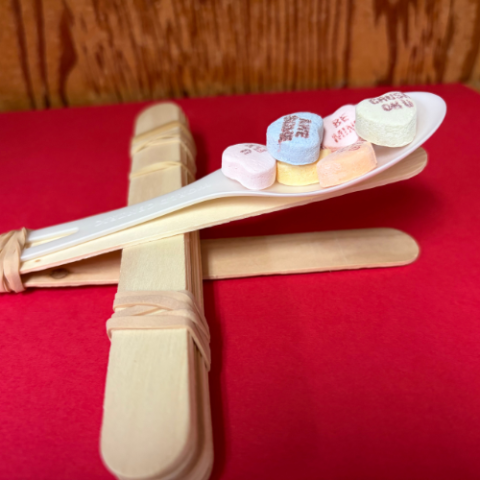 Heart shaped candy on a wooden catapult.