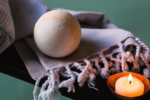white spherical bath bomb on a purple scarf next to a lit tea light