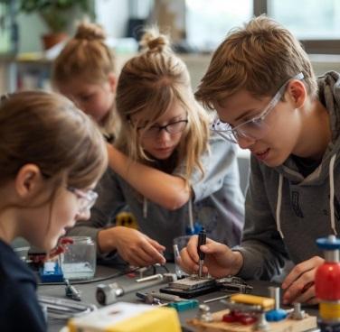 Three children with protective glasses are gathered around technological equipment