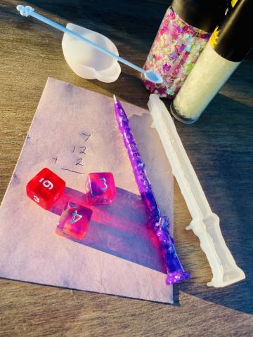 A piece of pink paper with numbers, three pink dice, and a pen that looks like a magic wand.