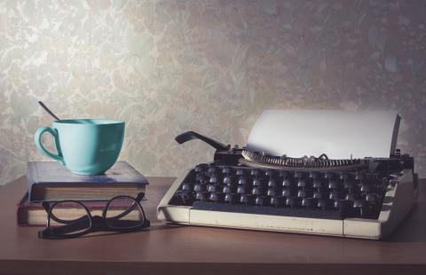 Image of typewriter and blue cup on top of a book 