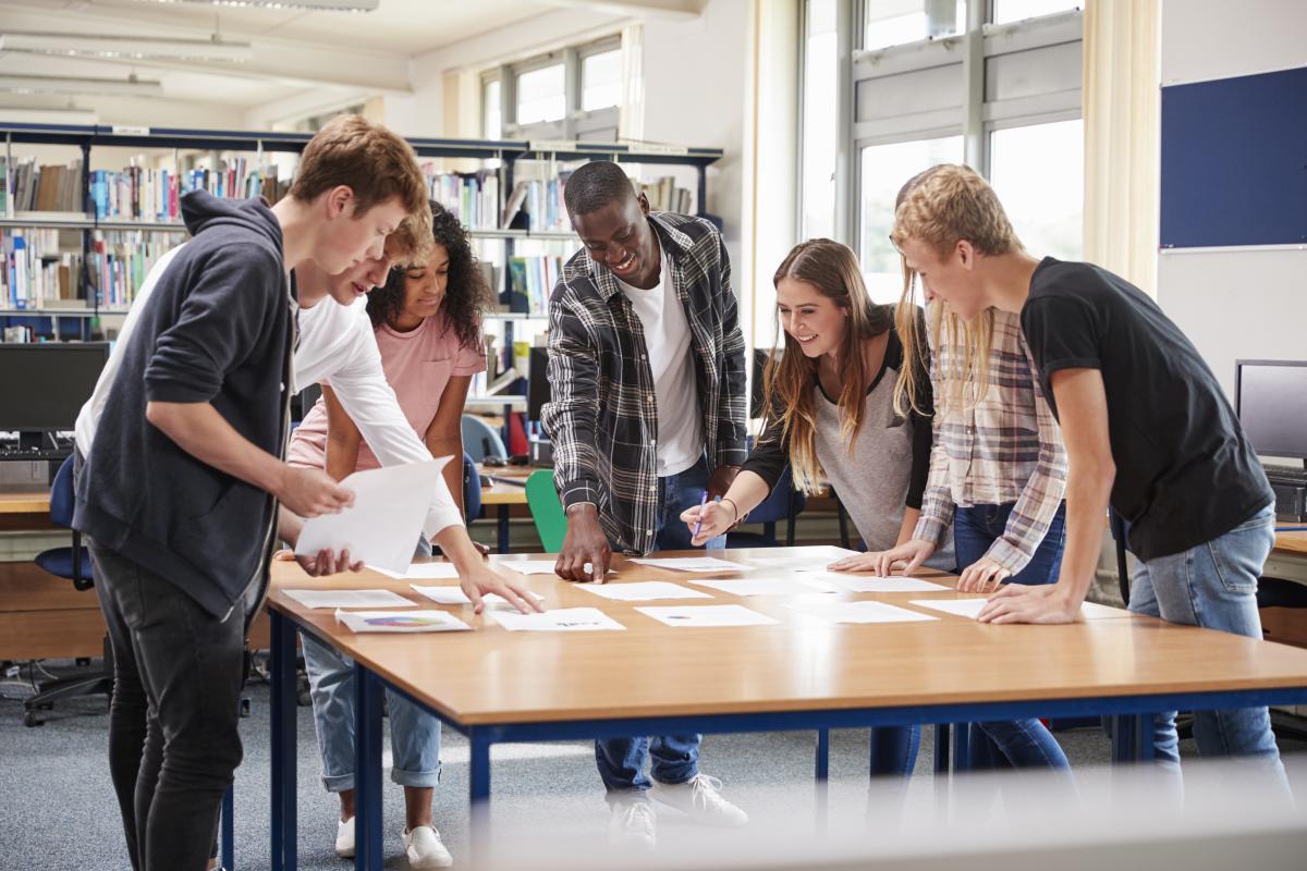 Five teens standing at a table working with papers.