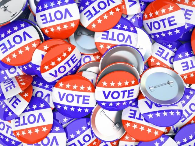 Pile of metal buttons in red, white, and blue, with the word "vote"