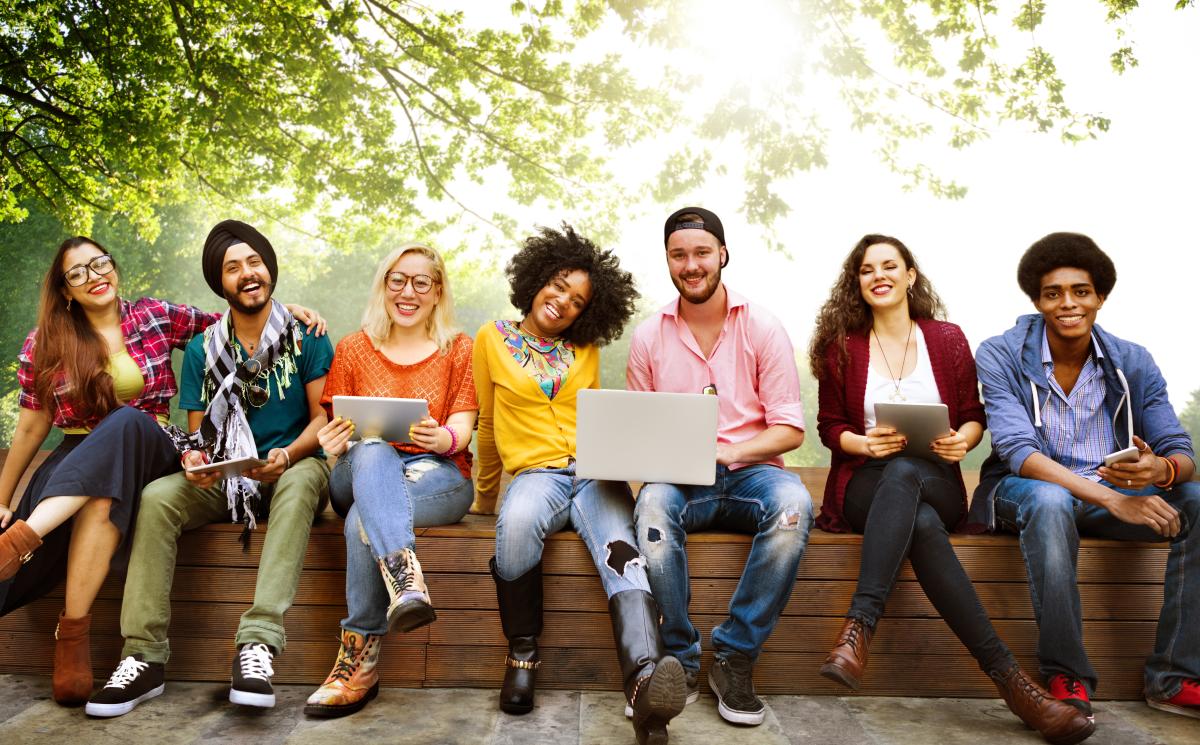 Seven Teens sitting on a wall with laptops, smiling.