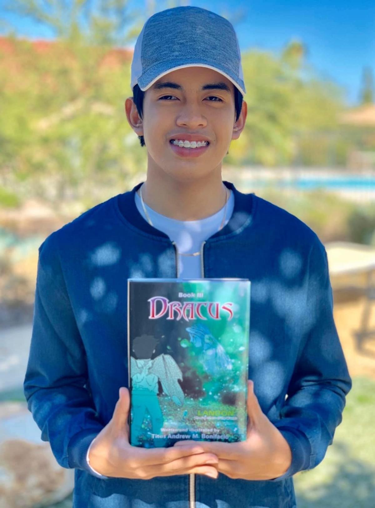 Smiling teen wearing a blue shirt and hat holding a book