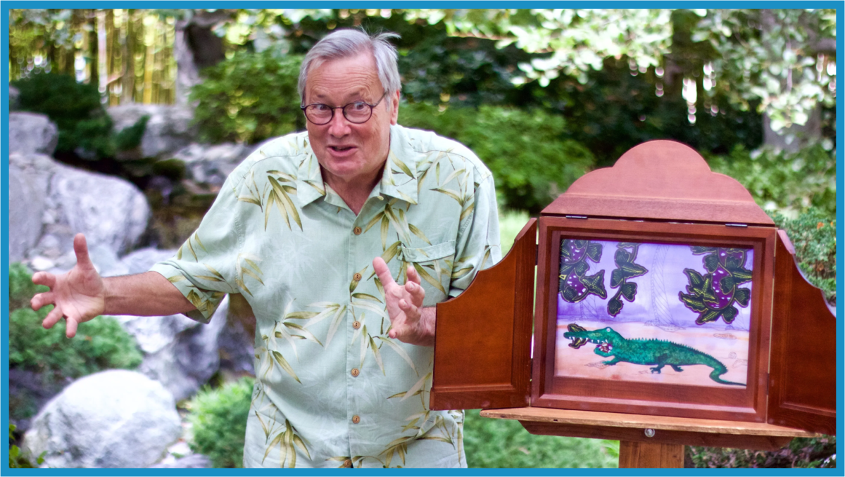 A man with an animated expression gestures with his hands as he tells the story of the dragon pictured in a storytelling box next to him