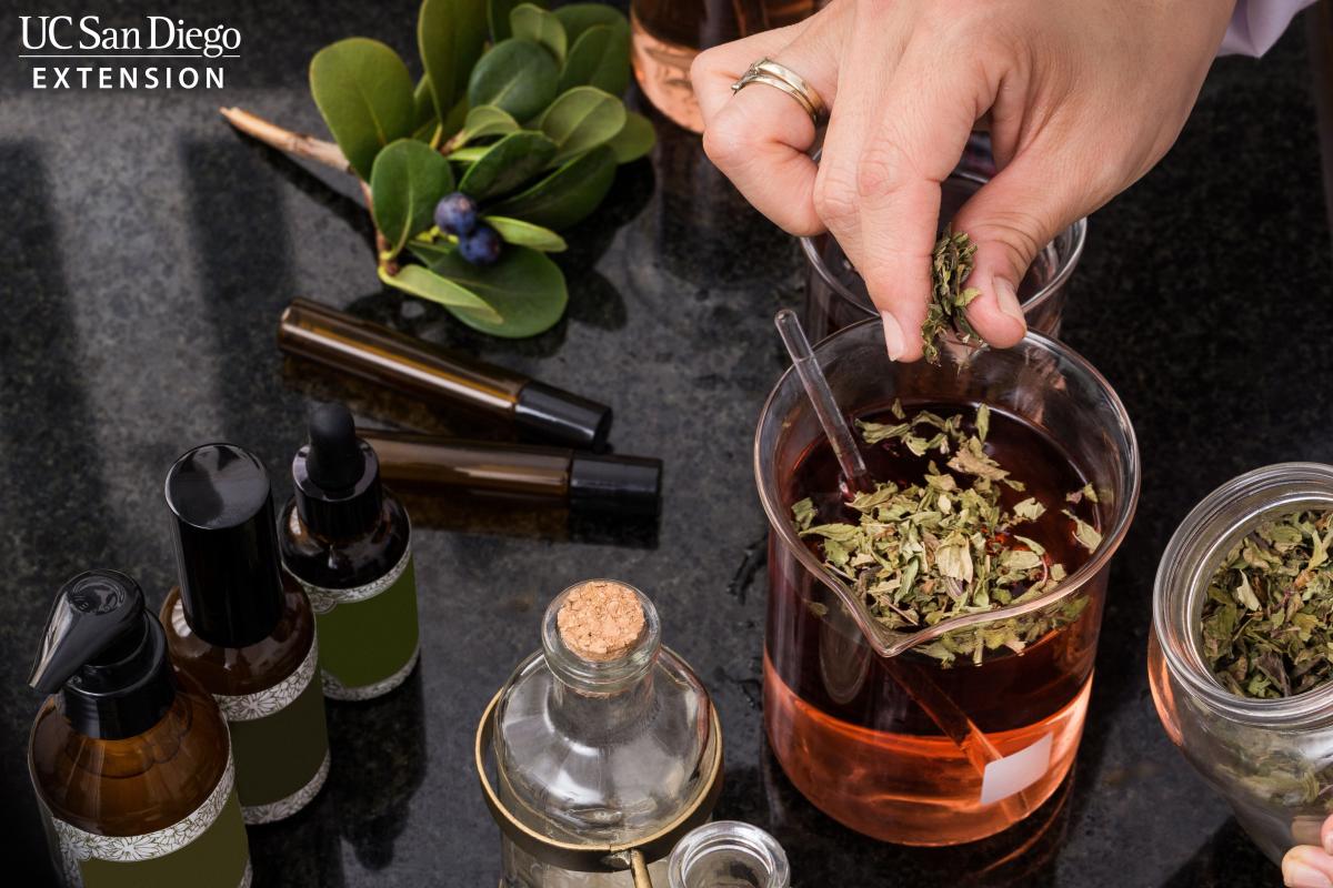 Person putting herbs into a vial with liquid on a desk.