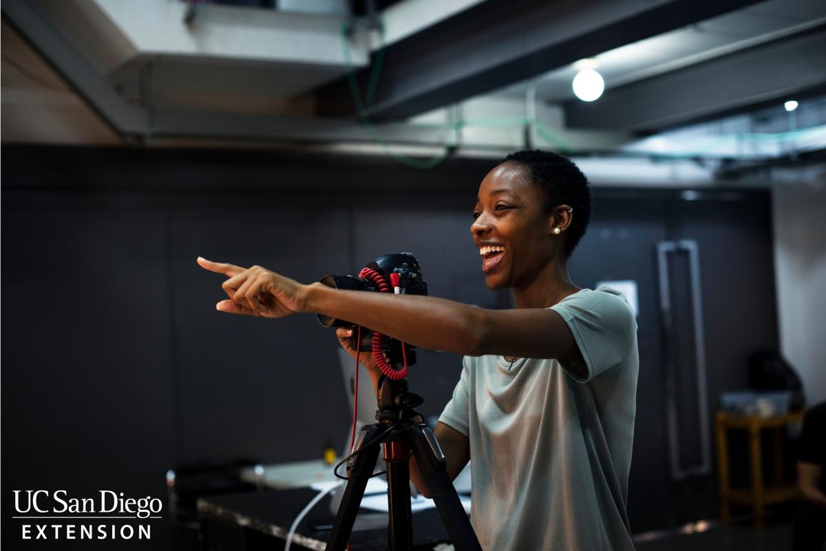 Student standing behind a camera pointing.