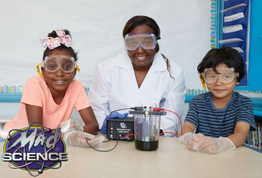 Woman and two children wearing protective goggles standing over a beaker
