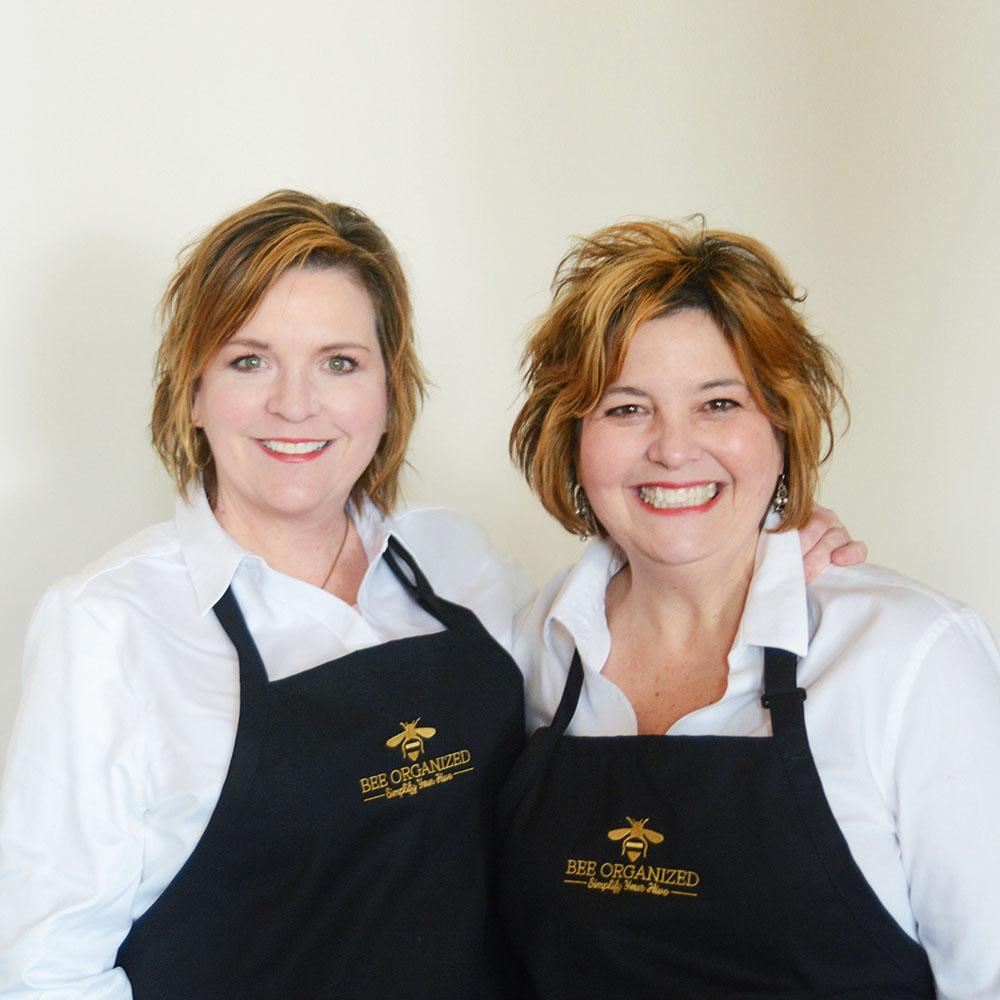 Two women wearing "Bee Organized" aprons