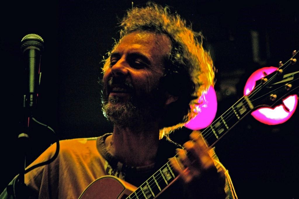 Photo of guitarist Peter Sprague, with a purple light shining behind him. 