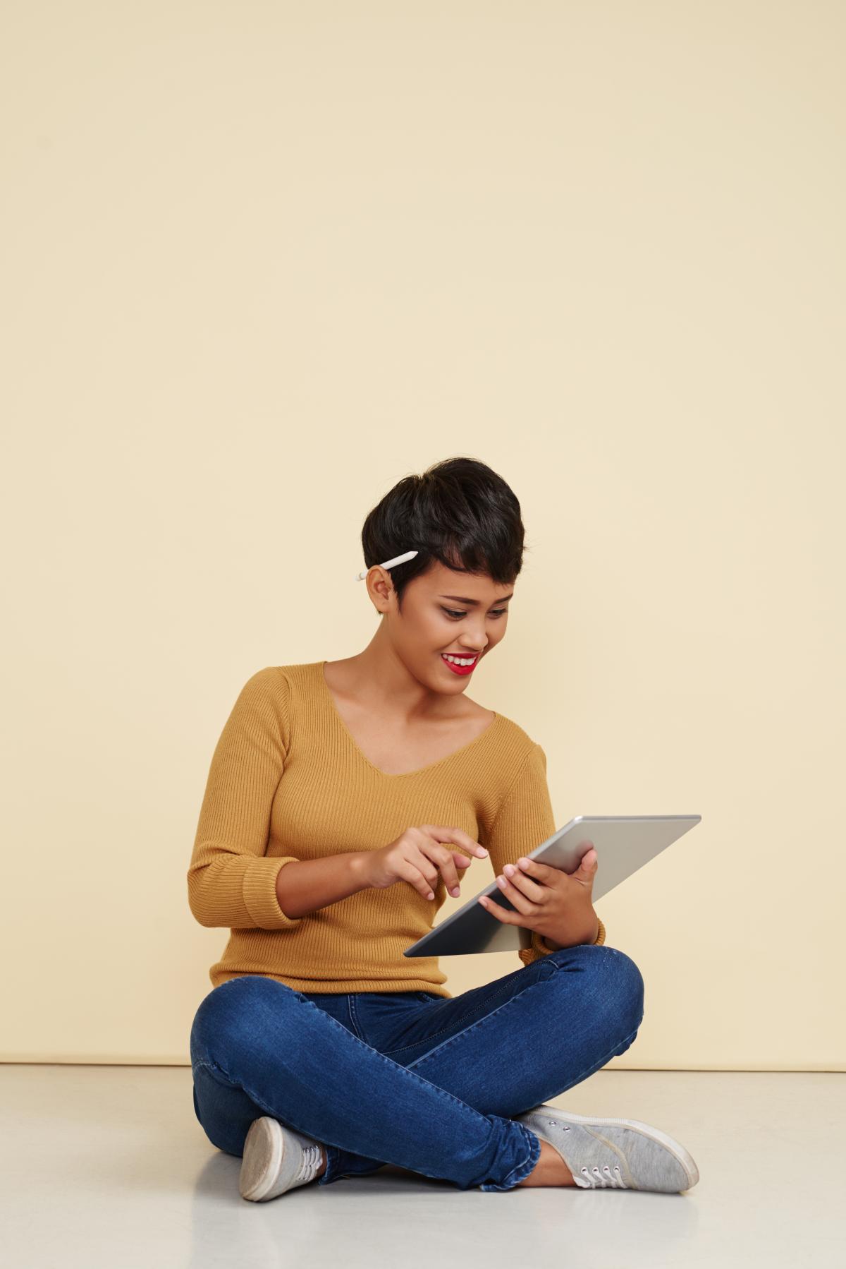 A woman sits while using an electronic tablet.