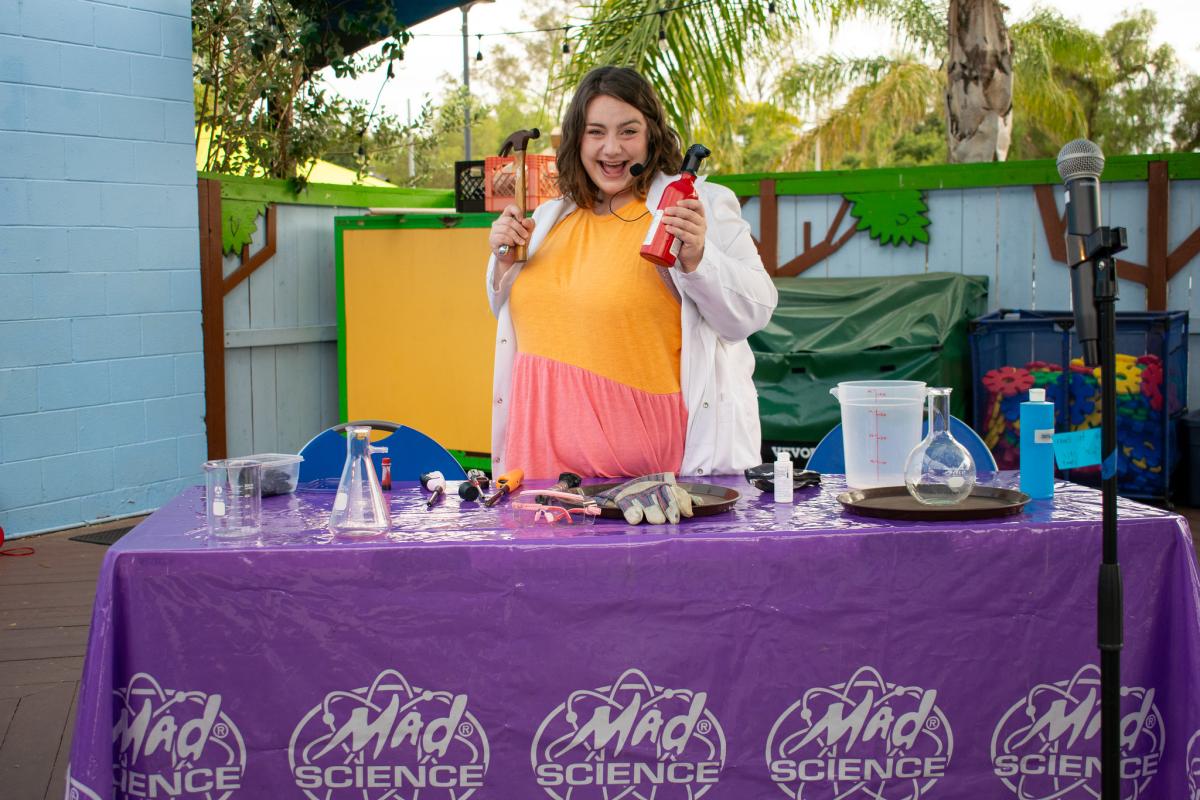 Smiling woman standing at table with science experiment supplies.