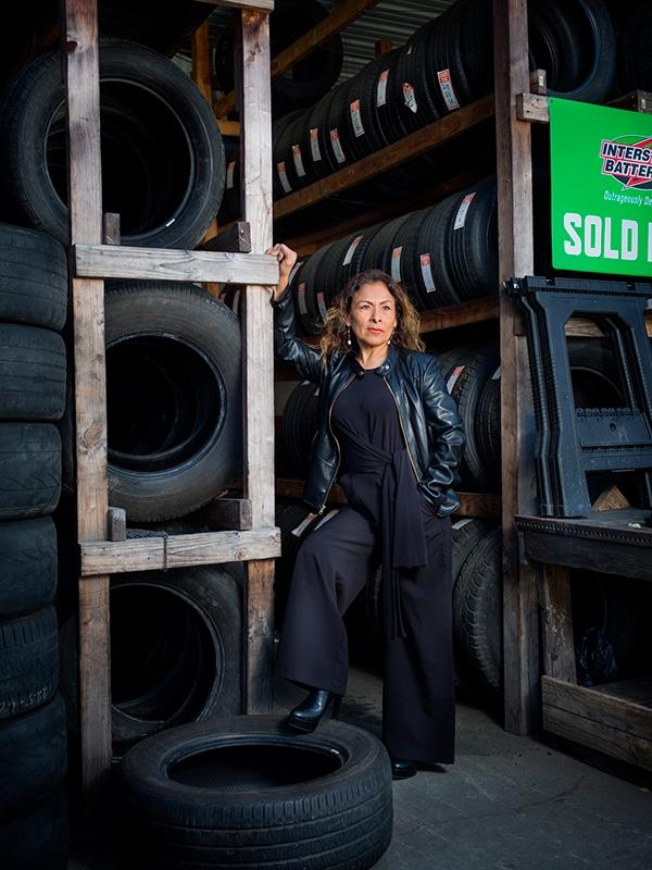 Photographic portrait of a woman posing in front f her tire store by artist John Raymond Mireles.