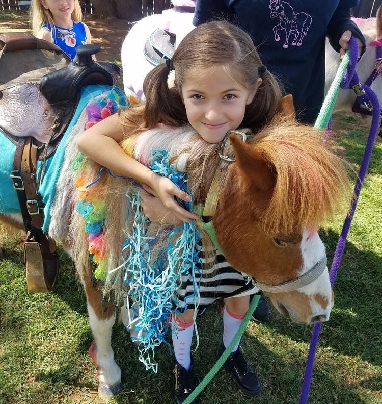 Girl hugging a brown and white pony that is dressed up with a flower lei and streamers.