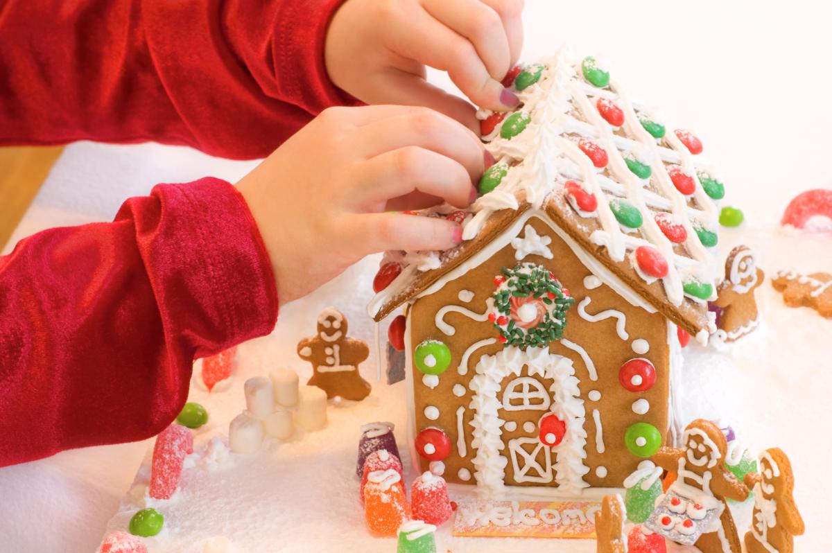 Child's hand decorating a gingerbread house