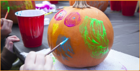 the hands of a child painting a pumpkin