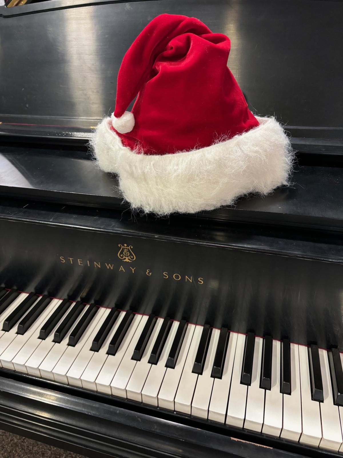 Santa hat sitting atop a black grand piano, focusing on the piano keys.