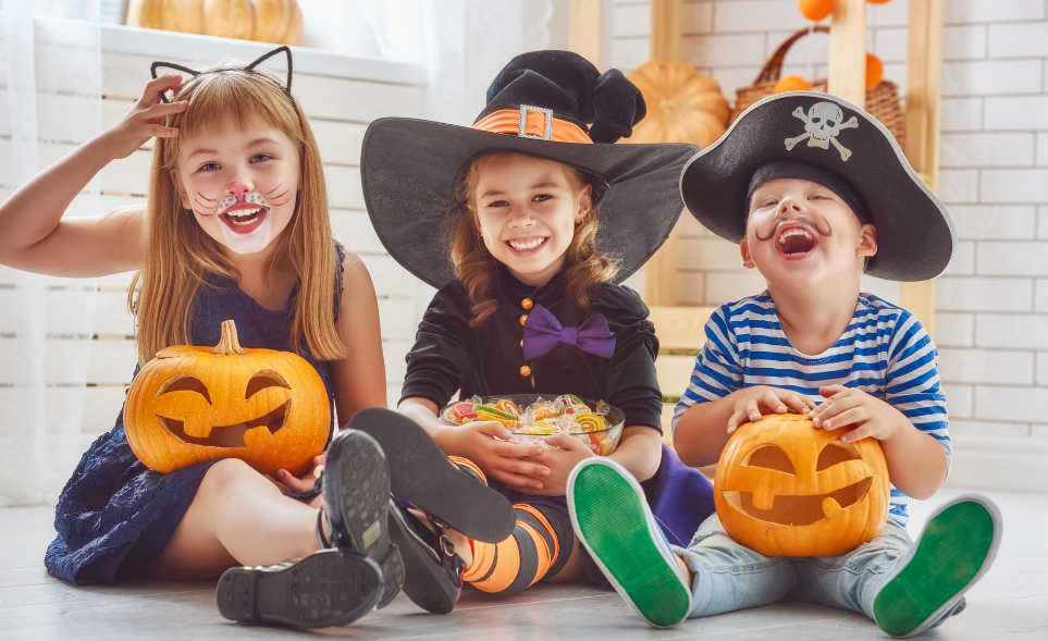 Three kids sit with jack-o-lanterns and costumes