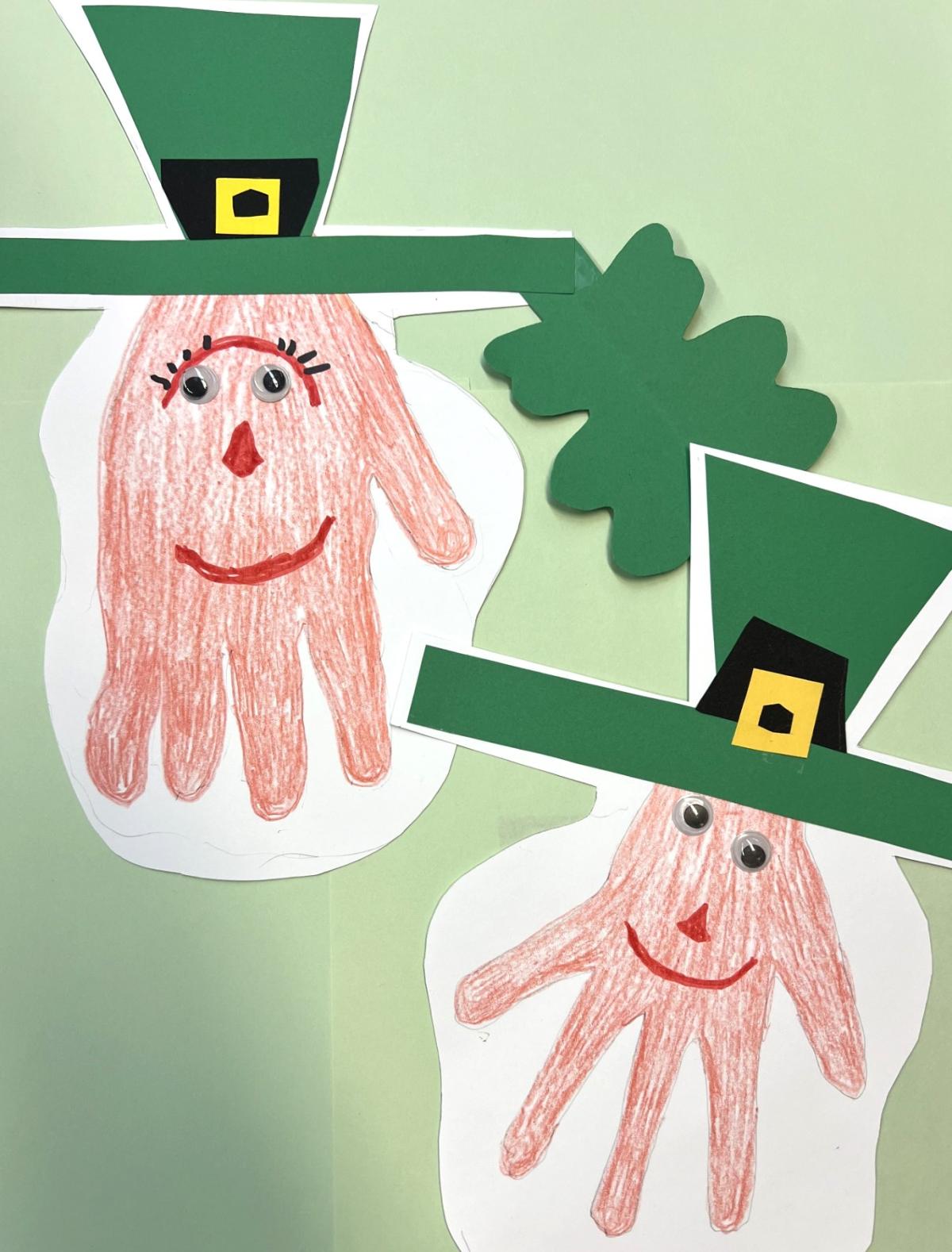 Paper crafts of colored in outlines of hands with faces drawn on. Green hats glued on.
