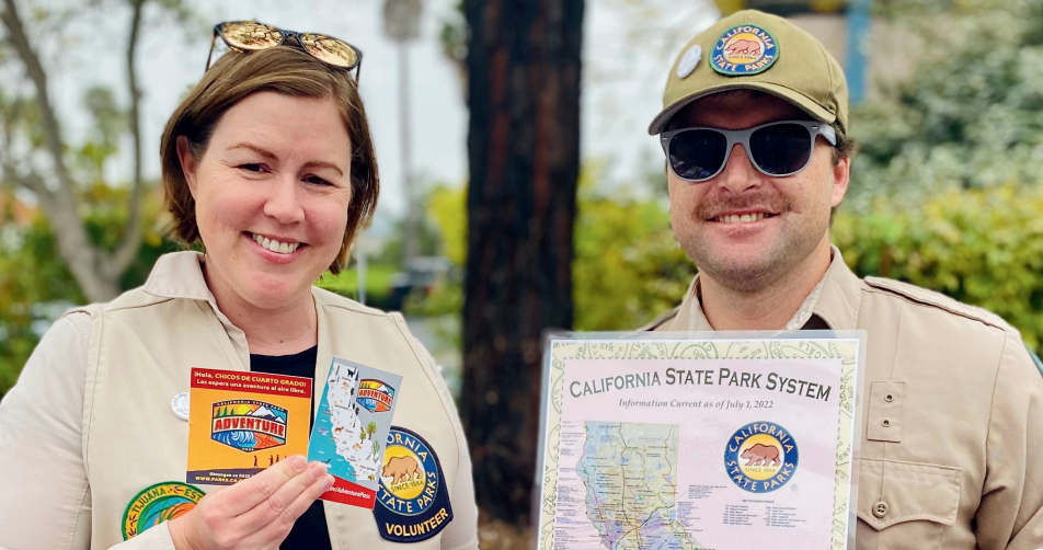 Two California State Park Rangers smiling at the camera and holding up California maps.