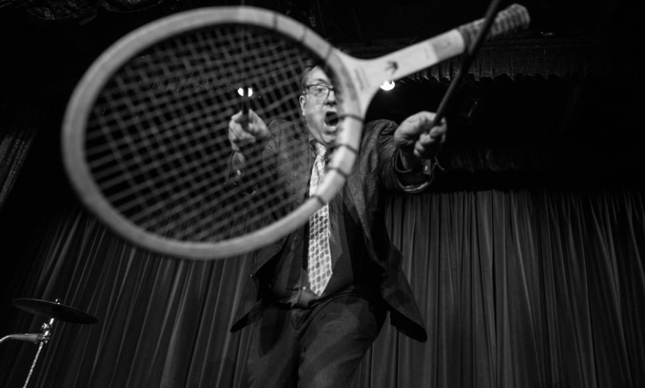 Michael Rayner juggling a tennis racquet with drumsticks.