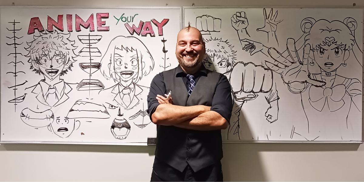 Anime artist standing in front of white boards with anime drawings