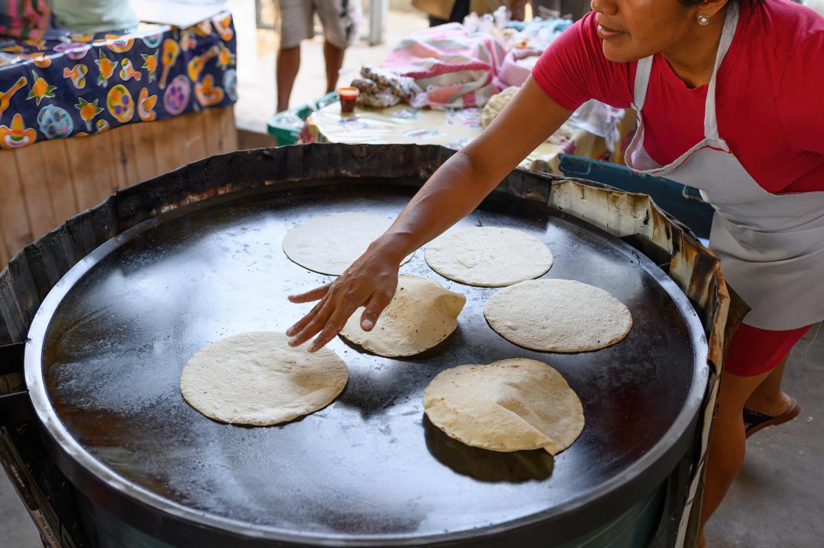woman wearing apron cooking six large tortillas on a large round pan