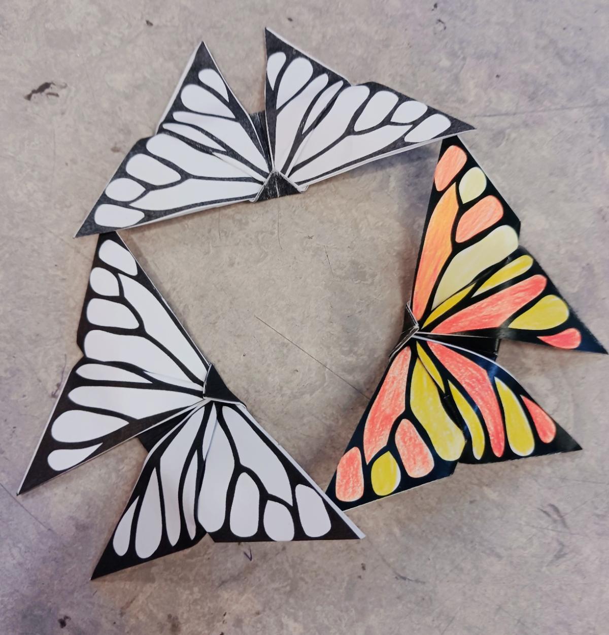 3 butterflies with wing tips touching, one is colored orange and yellow