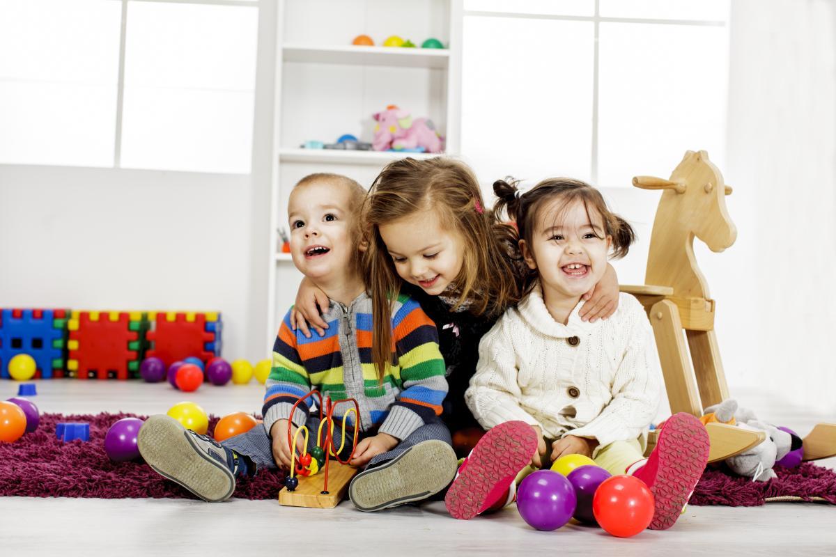 Three toddlers sitting on ground surrounded by toys.