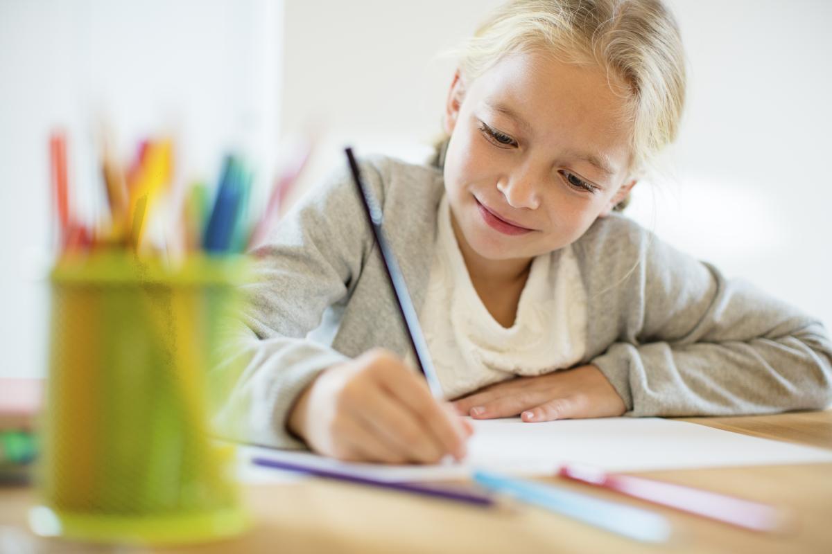 Blonde-haired child, about age 10, doing homework at a desk.
