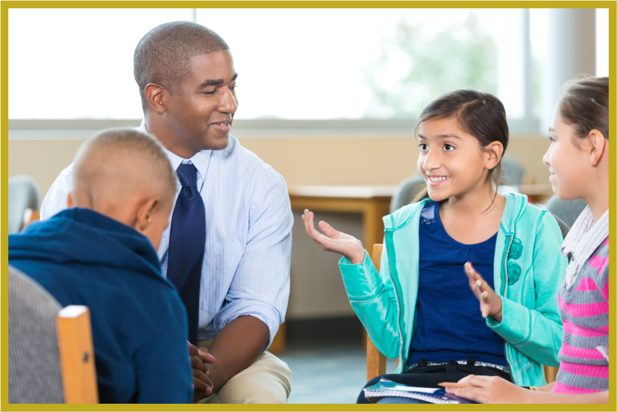 A young girl is smiling and talking to other children and an adult. They are all in a circle.