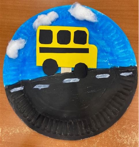 Paper school bus on a craft stick moving across paper plate background
