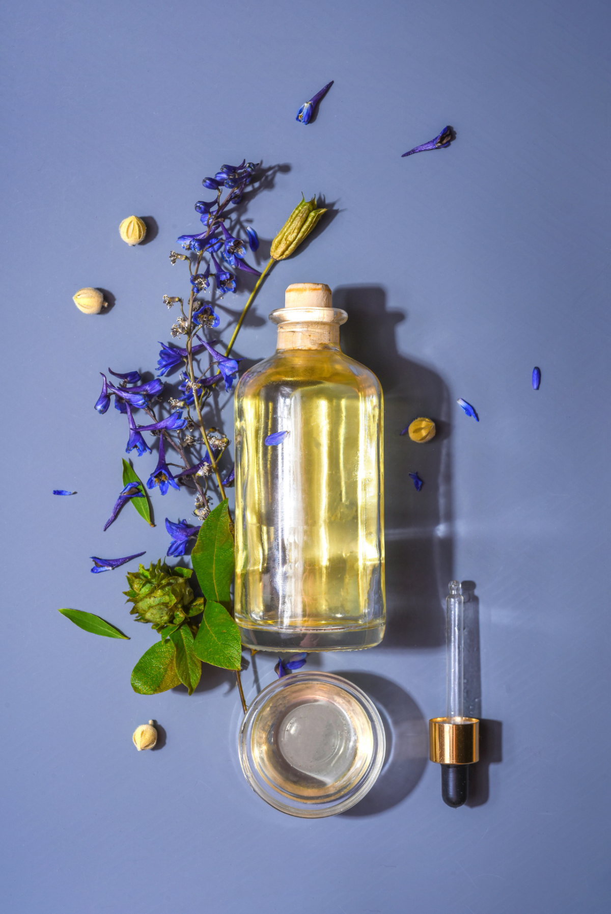 Photo of a glass bottle with a dropper, surrounded by flowers and herbs
