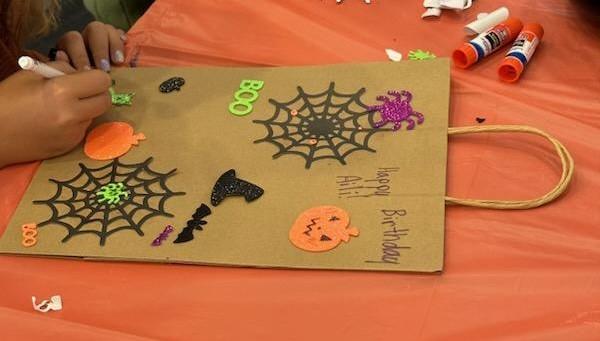 A child coloring a trick or treat bag that is decorated with stickers and paper spiderwebs