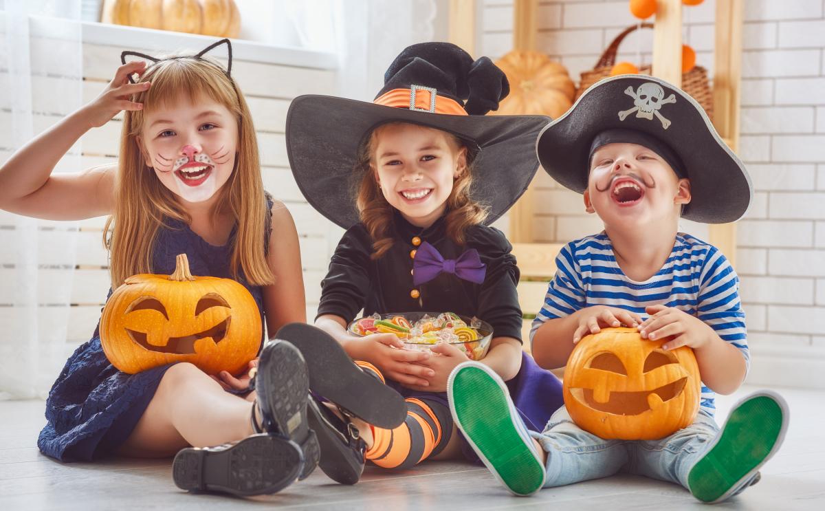 Three children sit in costumes with jack-o-lanterns