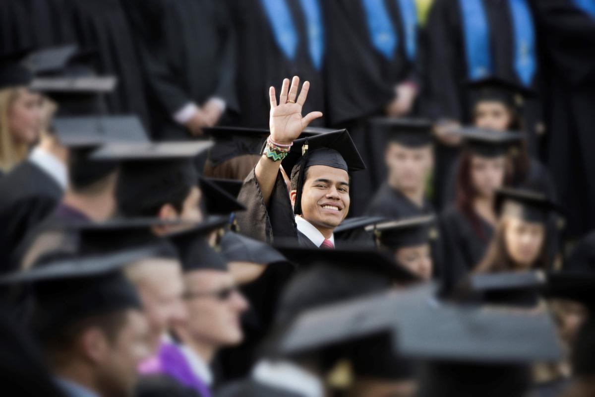 male student in graduation ceremony waving at camera above peers