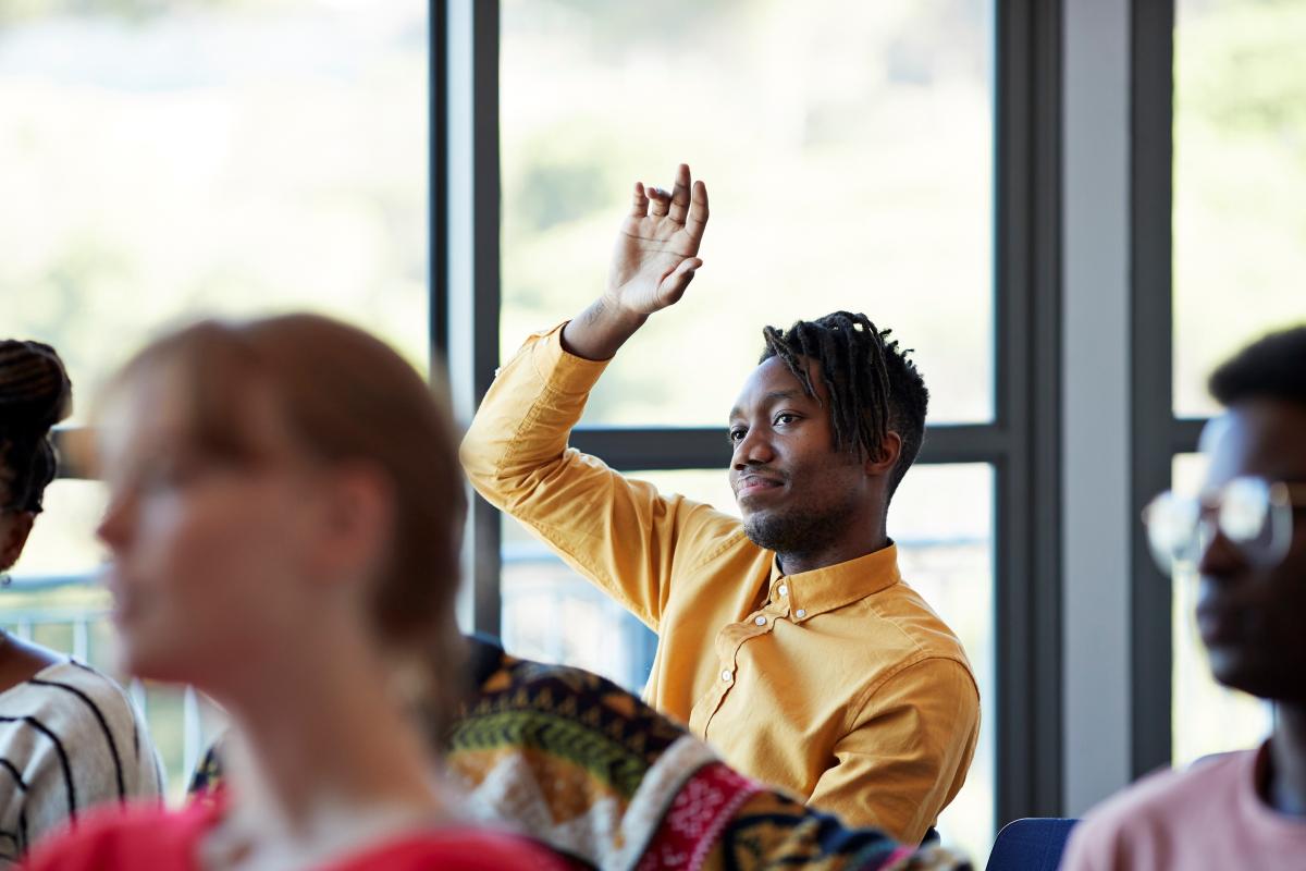 seated college student raising hand in classroom setting