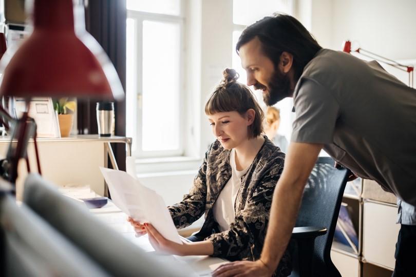 seated woman collaborating with standing man at angled desk