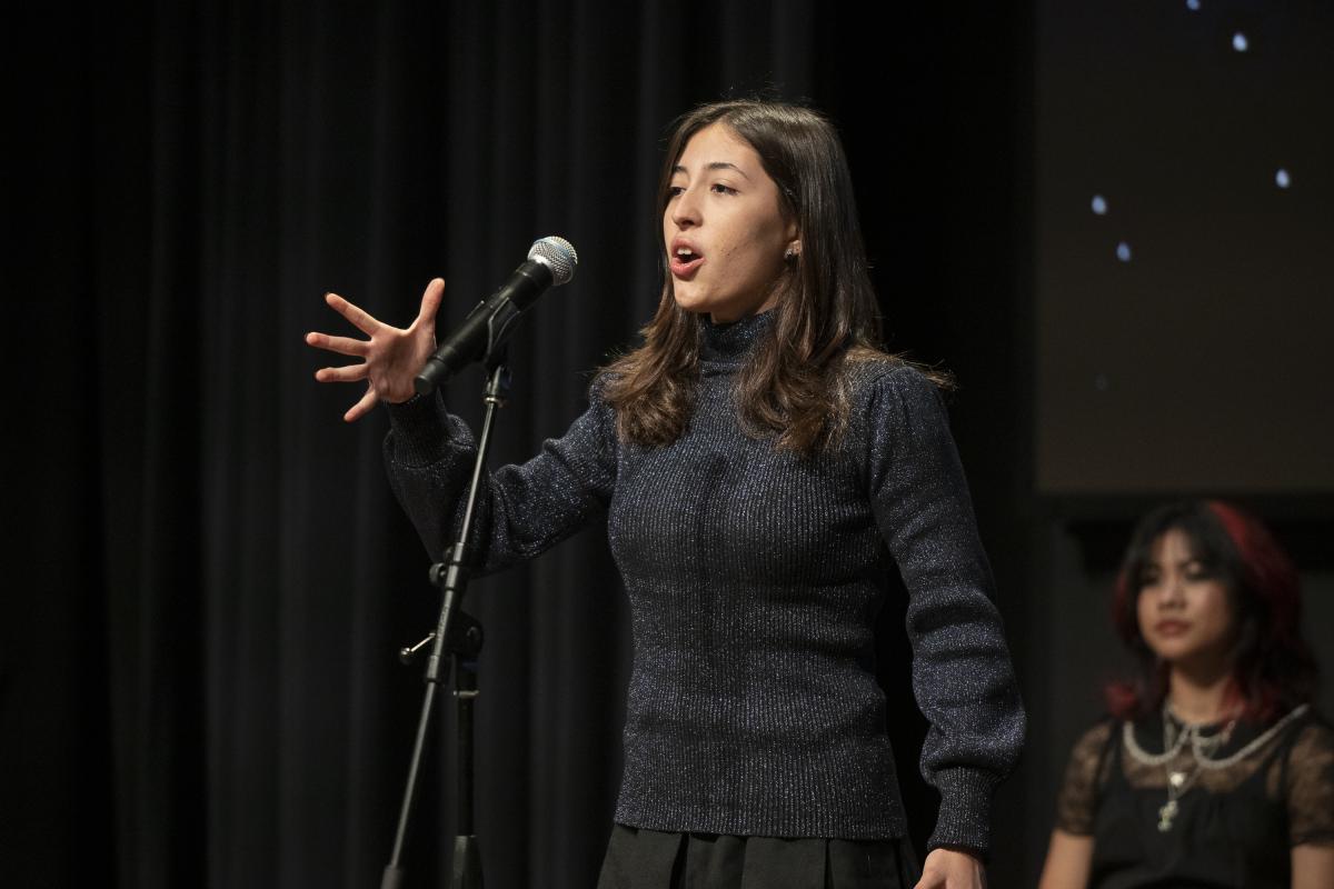 a young woman stands in front of a microphone to recite poetry