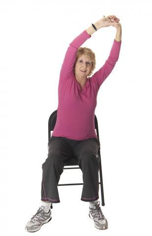 Women sitting on chair stretches arms over head.